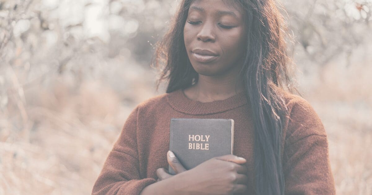 A woman holding her open Bible, grounding herself in God's word, for the Prayer & Perspective devotional "Don't Let Pressure Become Your Identity"