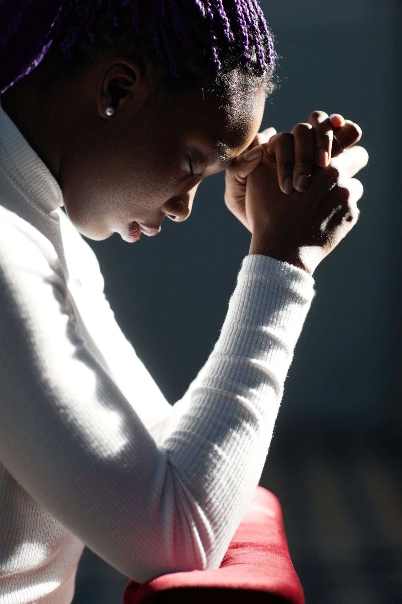 Close-up of a woman with bowed head and clasped hands in prayer.