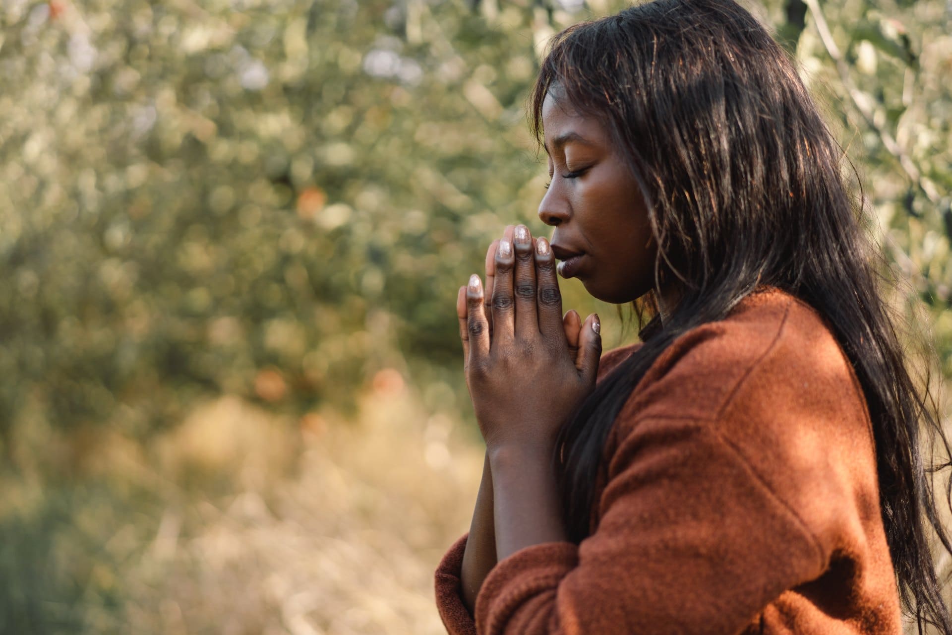 Woman outdoors with eyes closed and hands together near her face.