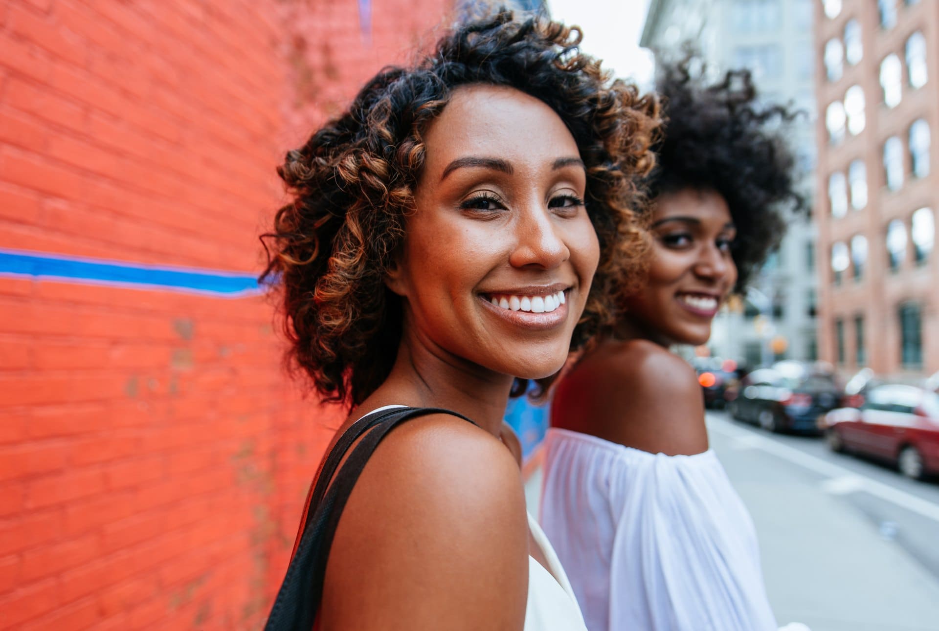 Two smiling women standing beside a colorful wall.
